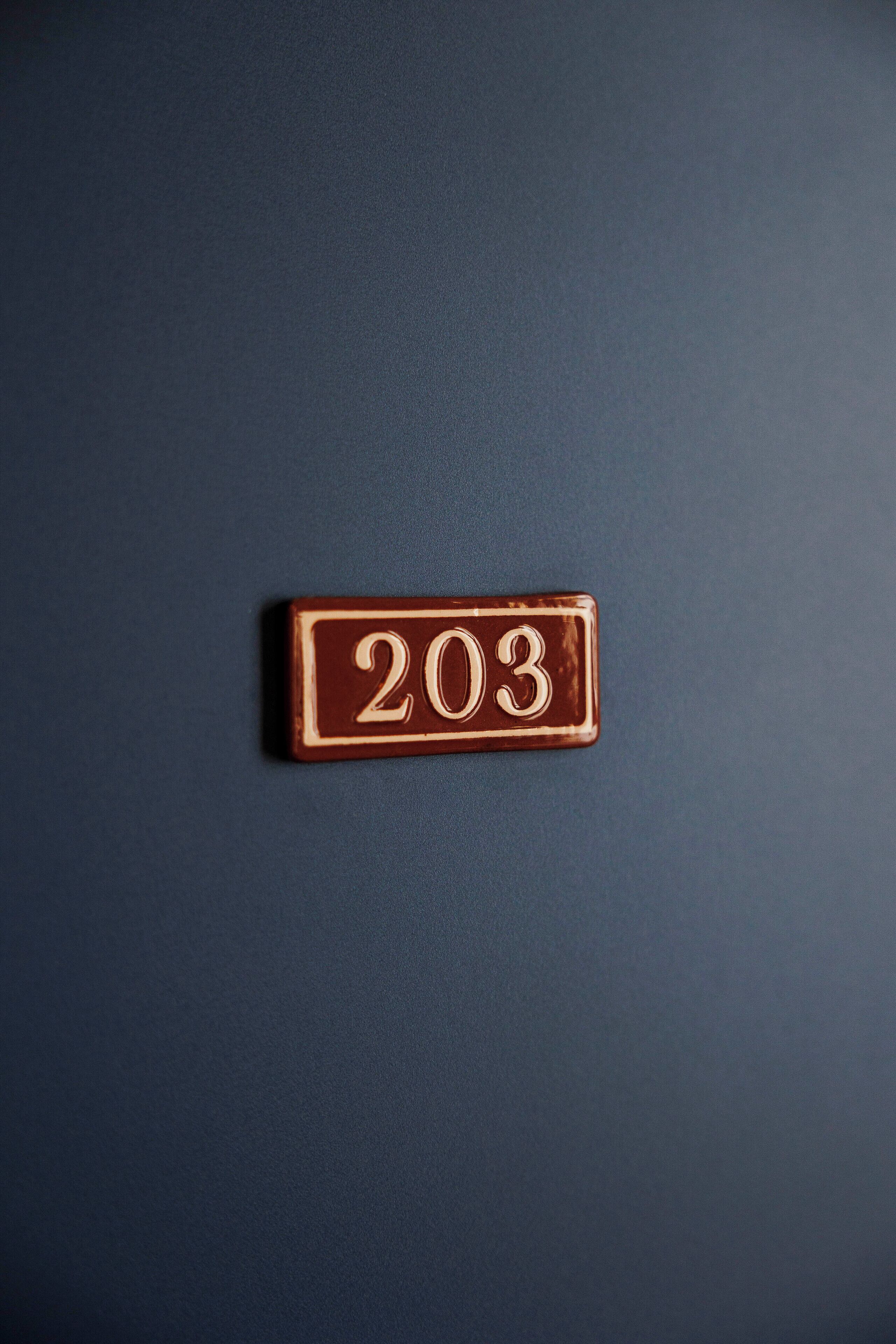 Pared azul escura com uma placa de latão retangular exibindo o número 203.
