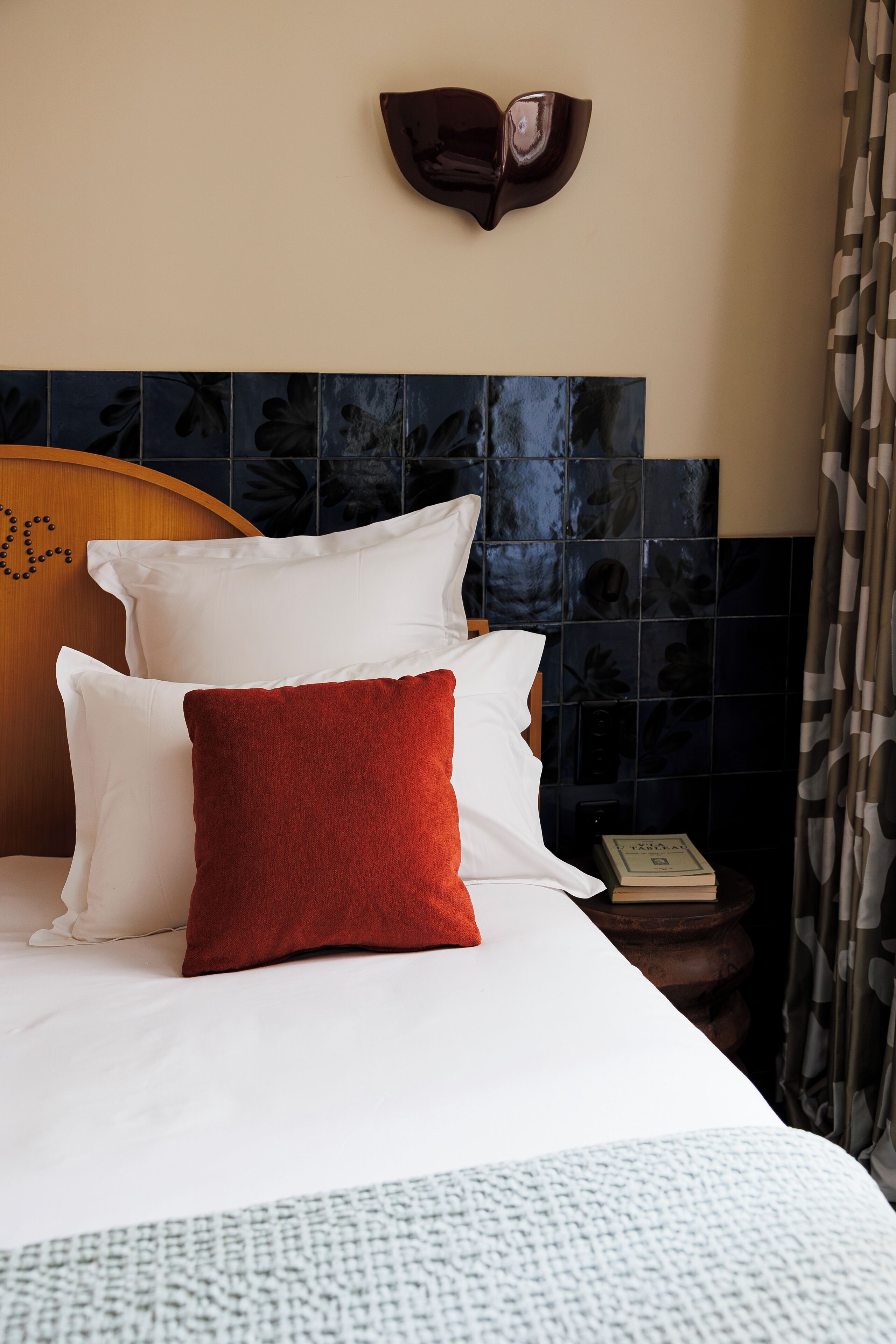 A neatly made bed with white and red pillows, a wooden headboard, and a decorative wall piece above it.