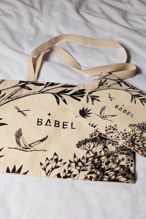 A beige tote bag with a bird and leaf pattern, the word "BABEL" printed on it, and a strap. - Babel Lille (Lille)