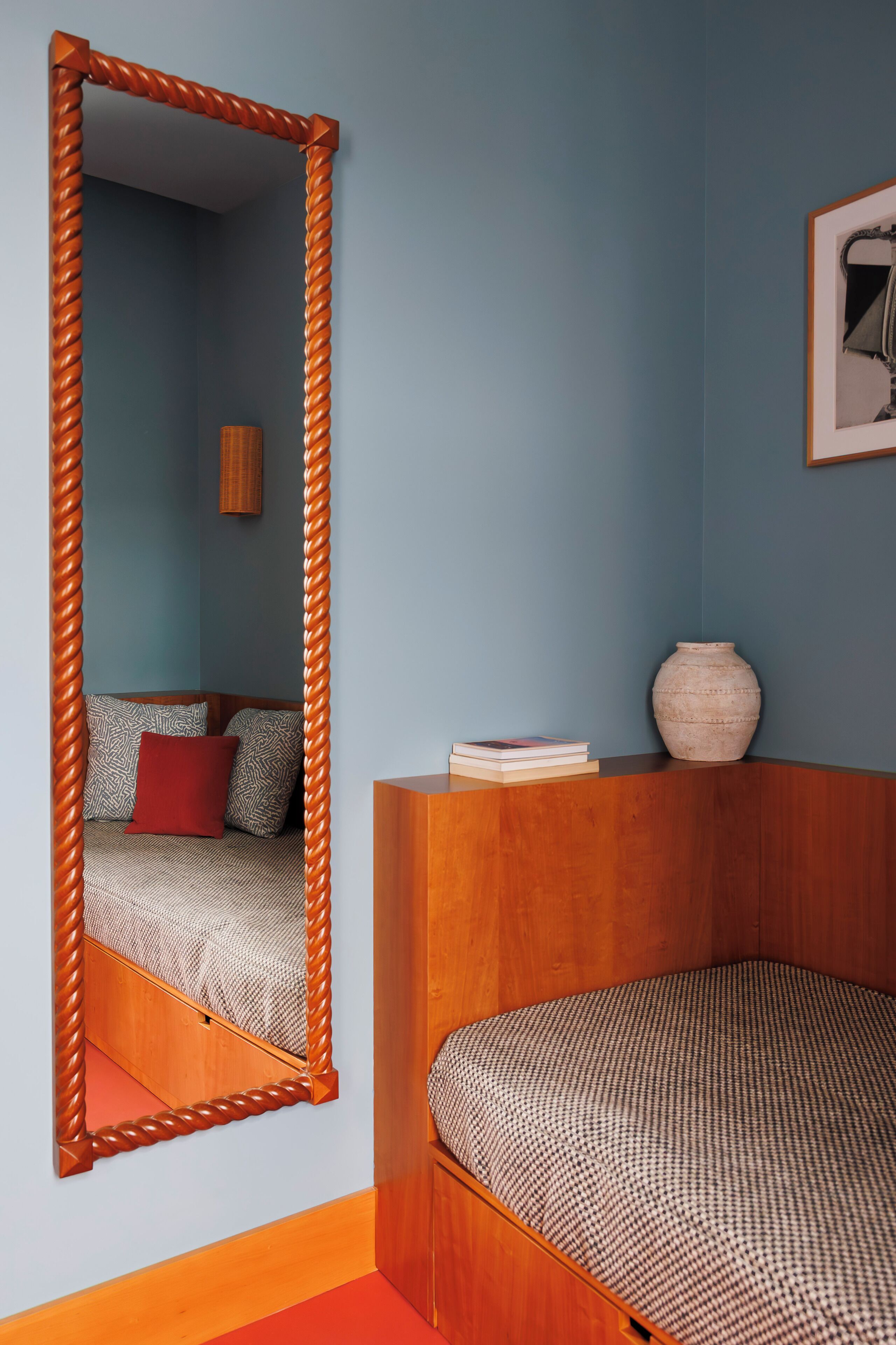 A bedroom with a wooden headboard, a large mirror, a bedside table with a vase, and a patterned bedspread.