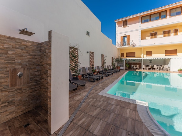 A poolside area with lounge chairs, a pool, and a building with balconies. - Comfy 4 Guest Apartment With Pool (Santa Teresa di Gallura)