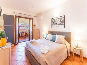 A hotel room with a bed, bedside lamps, a framed artwork, and a view through an open door to a balcony. - Comfy 4 Guest Apartment With Pool (Santa Teresa di Gallura)