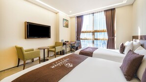 Une chambre d’hôtel avec deux lits, un bureau, une chaise, une télévision et une fenêtre avec des rideaux.