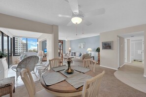 Un salon spacieux avec un coin repas, de grandes fenêtres et une vue sur l’extérieur.