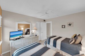 Quarto com duas camas, televisão, cômoda e ventilador de teto.