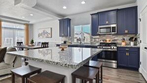 A modern kitchen with dark blue cabinets, stainless steel appliances, and a granite island with bar stools. - Heber Valley Escape w/ Games, Theater & Hot Tub (Heber City)