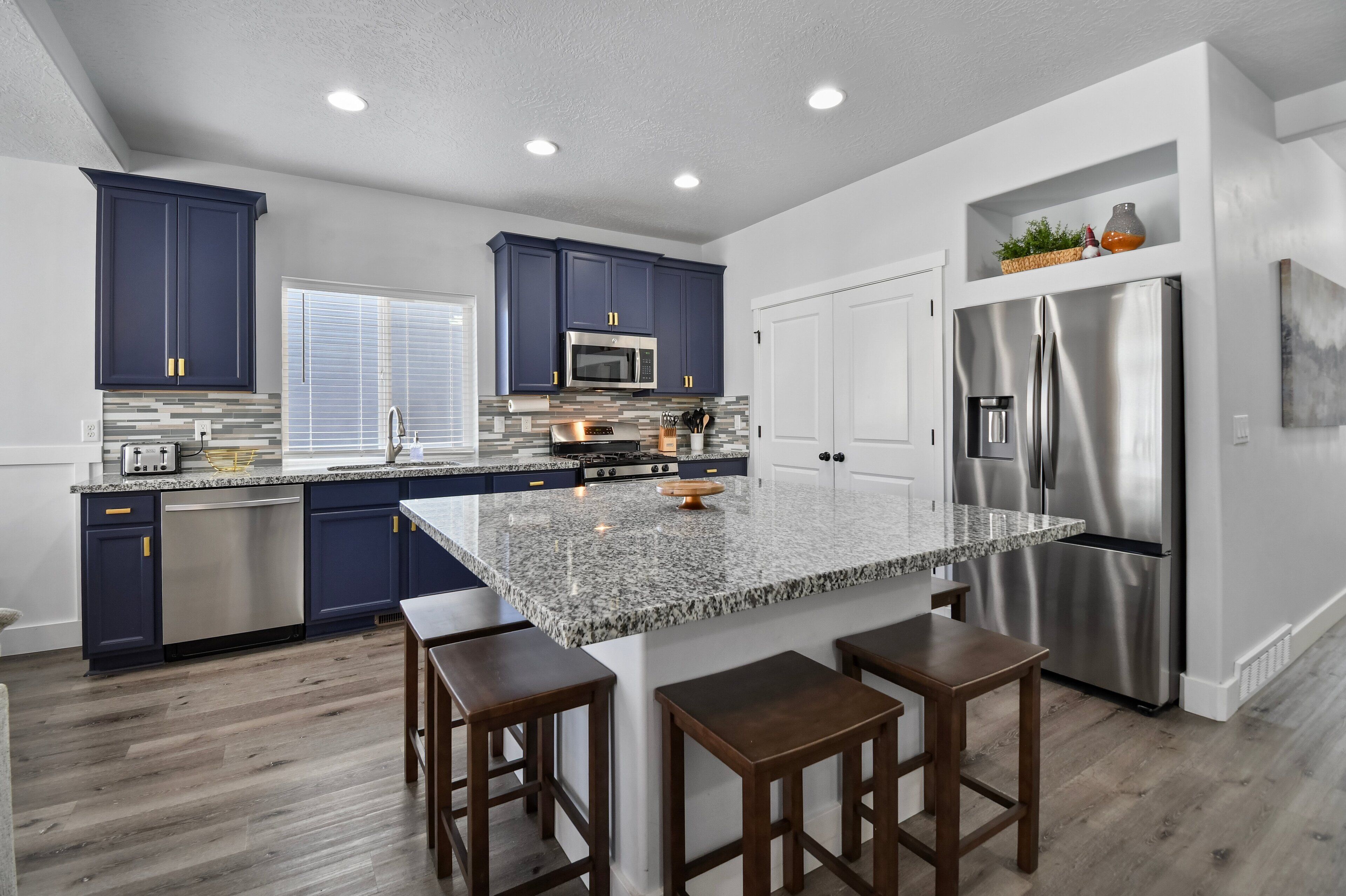 A modern kitchen with dark blue cabinets, stainless steel appliances, and a granite island with bar stools.