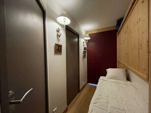 A narrow hallway leading to a bedroom with a bed, a door, and a wall-mounted light fixture. - Beautiful cozy apartment near slopes in Les Menuires with parking (Les Menuires)
