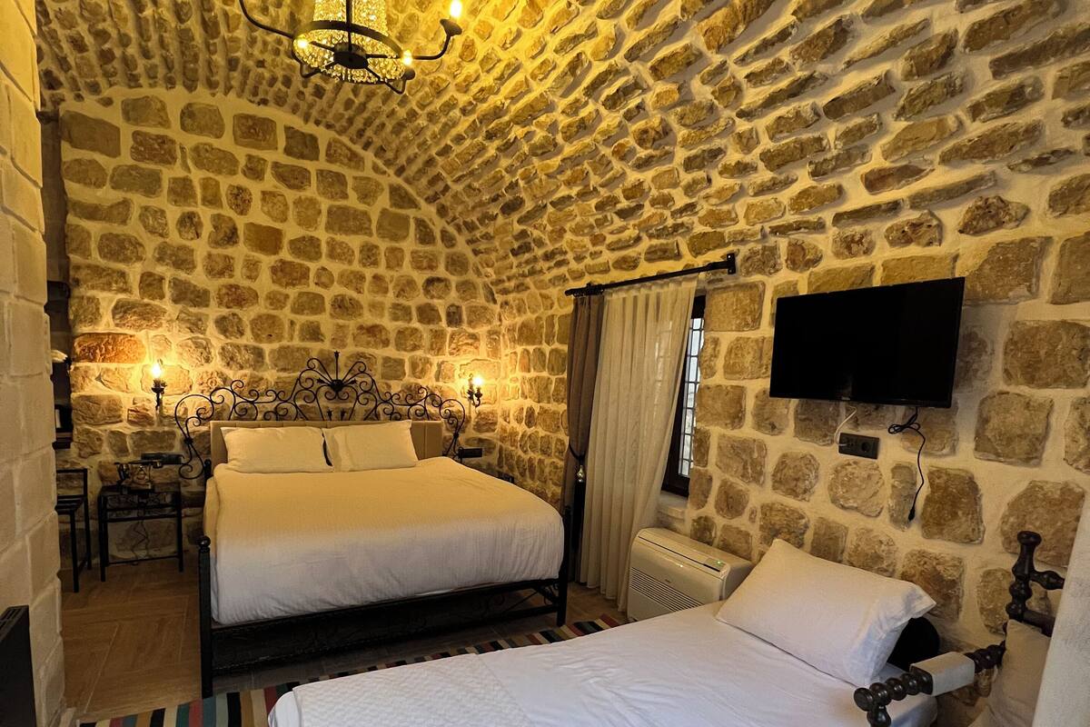 Une pièce chaleureuse avec des murs en pierre, deux lits, un téléviseur et un lustre.