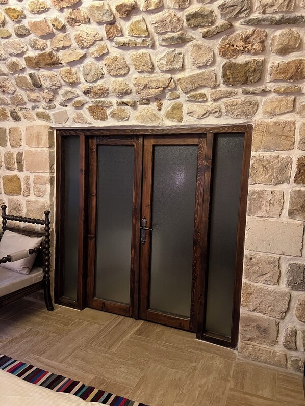 Una habitación con pared de piedra, un banco de madera y un juego de puertas dobles con paneles de vidrio esmerilado.