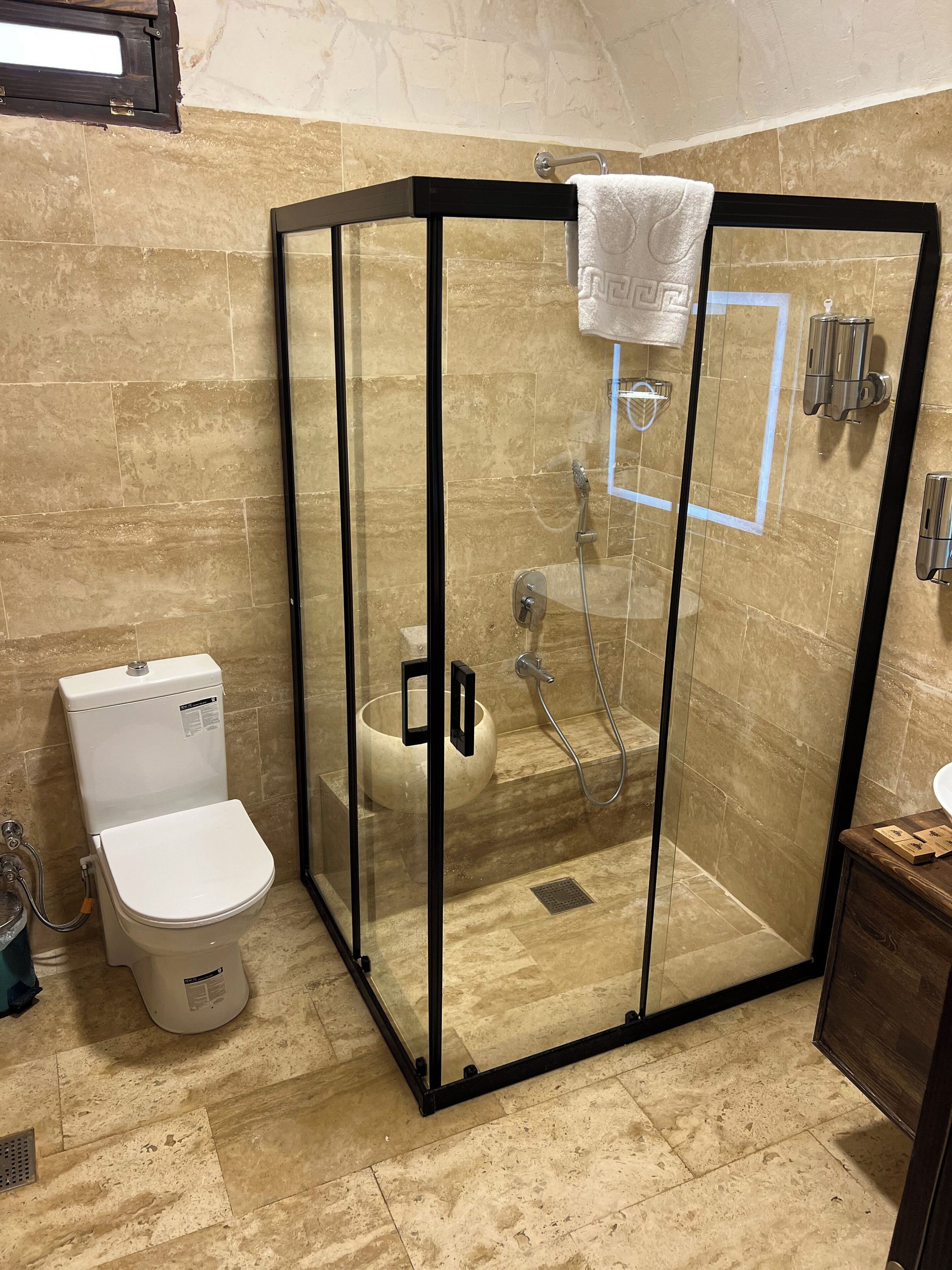 Eine Duschkabine mit Toilette und Waschbecken in einem Badezimmer mit beige gefliesten Wänden.