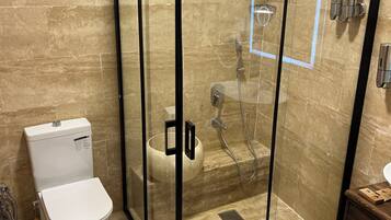 Eine Duschkabine mit Toilette und Waschbecken in einem Badezimmer mit beige gefliesten Wänden.