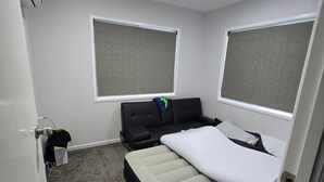 Un dormitorio pequeño con cama, un rincón de descanso y dos ventanas.