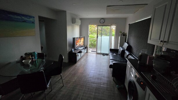 Una cocina moderna con lavadora, una zona de comedor con mesa de vidrio y un televisor al fondo.