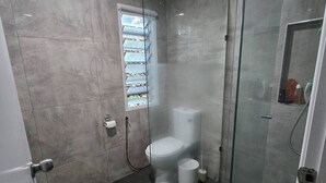 Un baño moderno con ducha envuelta en vidrio, inodoro y una pequeña ventana.