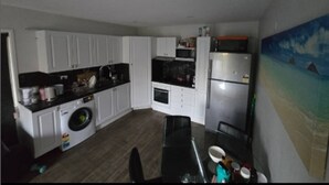 Una cocina compacta con alacenas blancas, lavadora, microondas y refrigerador.