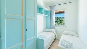 A bedroom with two beds, a wardrobe, and a window with a view of a forest. - Complex Surrounded by Greenery With Pool (Arzachena)