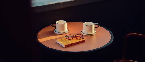 A table with two cups and a pair of glasses on a round table, with a view of buildings through a window.
