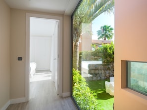 A hallway leading to a room with a view of a garden and a stone wall.