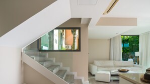 A modern interior with a staircase, a living area with a sofa, and a view of greenery outside.