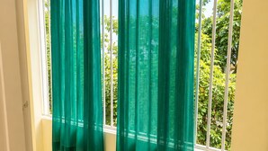 Ein Zimmer mit einem großen Fenster, grünen Vorhängen und einem gefliesten Boden.