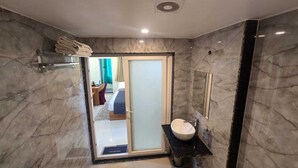 A bathroom with a marble wall, a sink, a mirror, and a shower area. - Hotel Vindhya Ganga Inn (Varanasi)