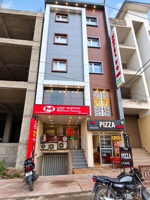 A multi-story building with a ground-floor restaurant named 'The Pizza Cafe' and a visible sign for 'Muthoot Finance' on the left. - Hotel Vindhya Ganga Inn (Varanasi)