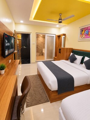 A hotel room with a bed, a desk, a TV, a bathroom, and a ceiling fan. - Hotel Vindhya Ganga Inn (Varanasi)