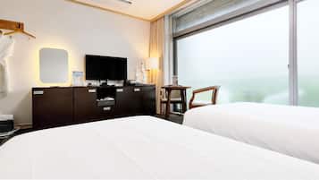 Quarto de hotel com cama, televisão, escrivaninha com abajur, cadeira e janela com vista.
