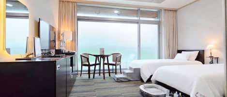 Habitación de hotel con escritorio, dos camas, una silla, una mesita y vistas al exterior.