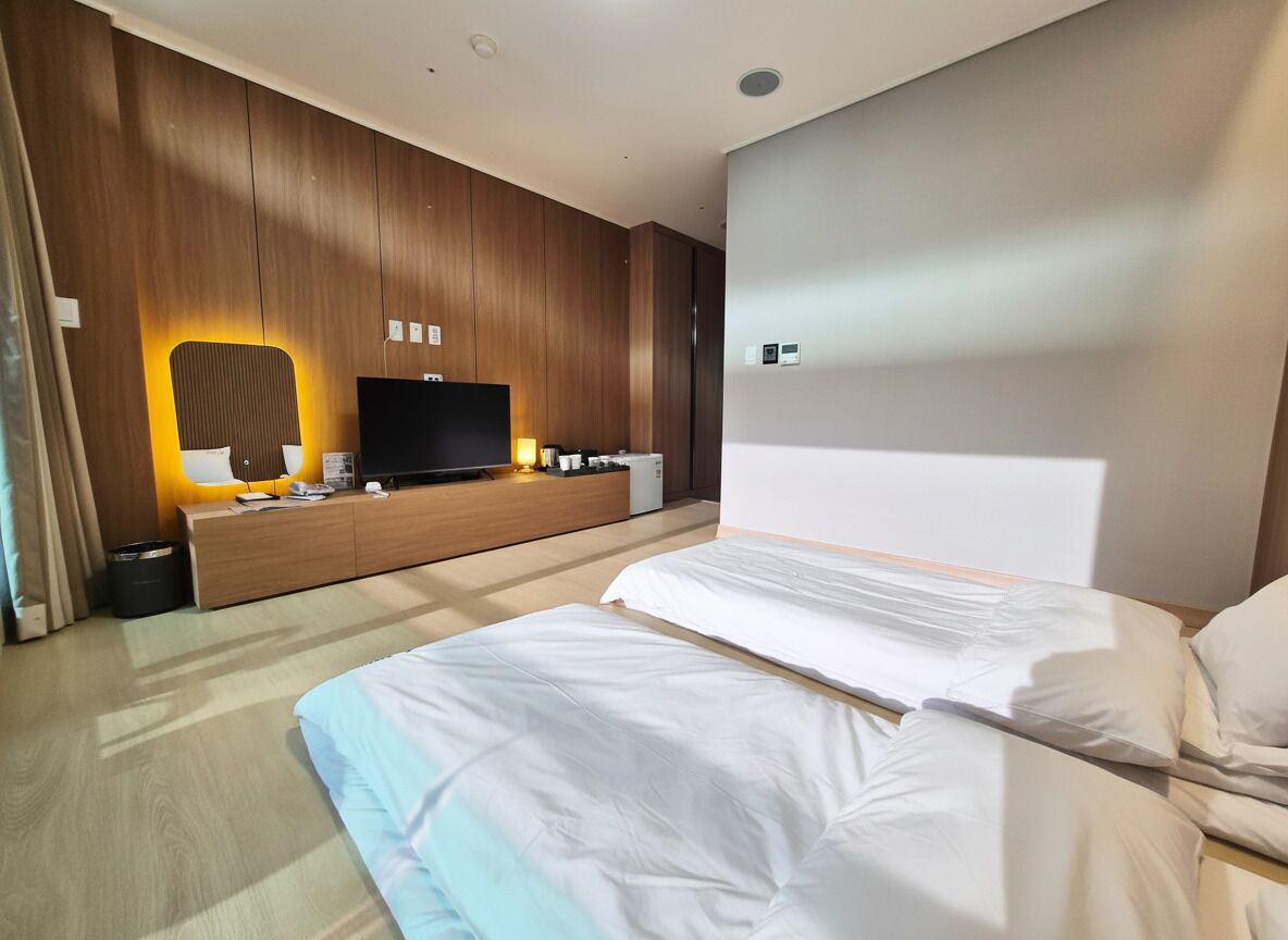 Ein modernes Hotelzimmer mit einem großen Bett, einem Fernseher, einer Wandpaneele aus Holz und einem Nachttisch mit Lampe.