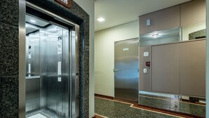 An elevator area with metallic doors, a control panel, and a fire alarm. - Building on the Beachfront in BC - Esas (Balneário Camboriú)