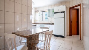 A kitchen with white cabinets, a granite countertop, and a refrigerator. - Building on the Beachfront in BC - Esas (Balneário Camboriú)