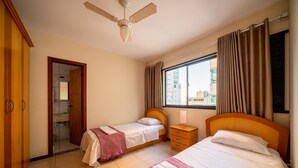 A hotel room with two beds, a ceiling fan, a window with curtains, and a view of the city. - Building on the Beachfront in BC - Esas (Balneário Camboriú)