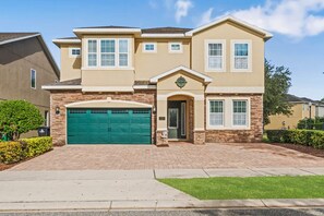 A two-story house with a green garage door, stone facade, and a well-maintained lawn. - Foosball, Ping Pong, Resort-style Pool: Sweet Spot (Kissimmee)