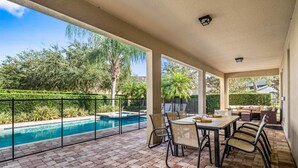 En overdækket terrasse med pool, udendørs møbler og udsigt over det omkringliggende grønne område.