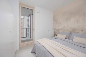 Ein Schlafzimmer mit Bett, Heizkörper, Tür und Blick auf Gebäude.
