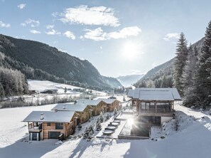 A snow-covered lodge with multiple wooden cabins and a glass-enclosed building, surrounded by snow-covered trees and mountains. - Chalets Valsegg (Rio di Pusteria)