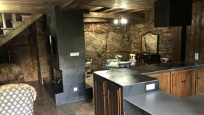 A kitchen with a central island, wooden cabinets, a stone wall, and a staircase.