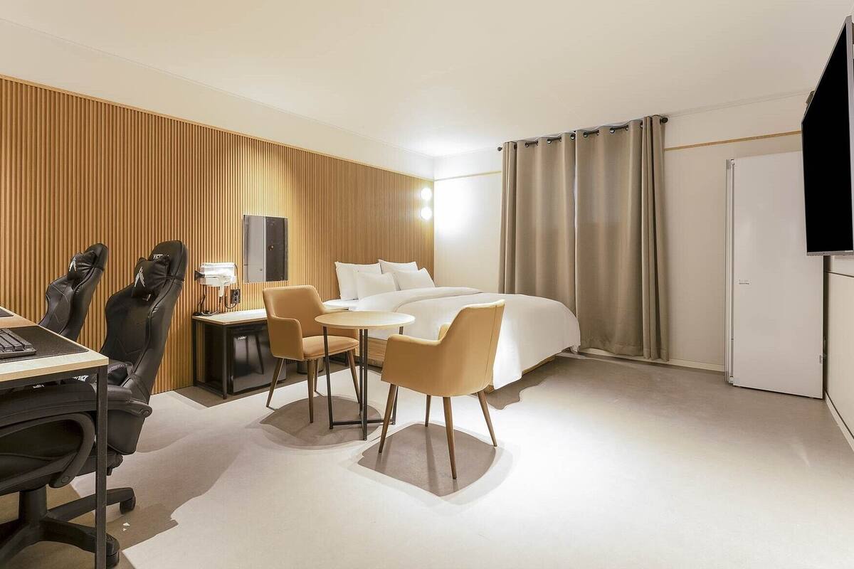 Habitación de hotel moderna con cama, escritorio, sillas y televisor.