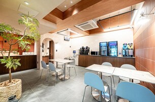 A modern cafe with a wooden ceiling, a central table with chairs, a coffee machine, and a refrigerator with drinks.