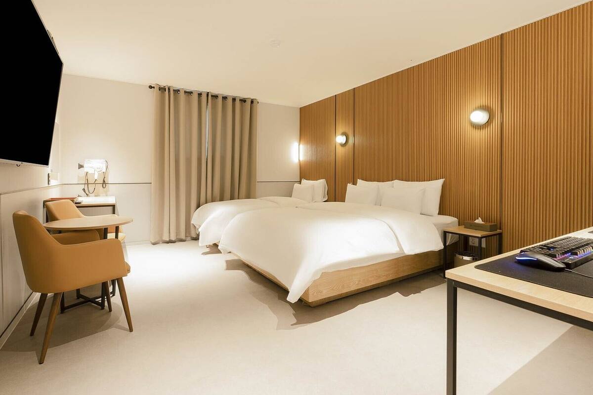 Habitación de hotel moderna con una cama grande, un escritorio con computadora, una silla y un televisor montado en la pared.