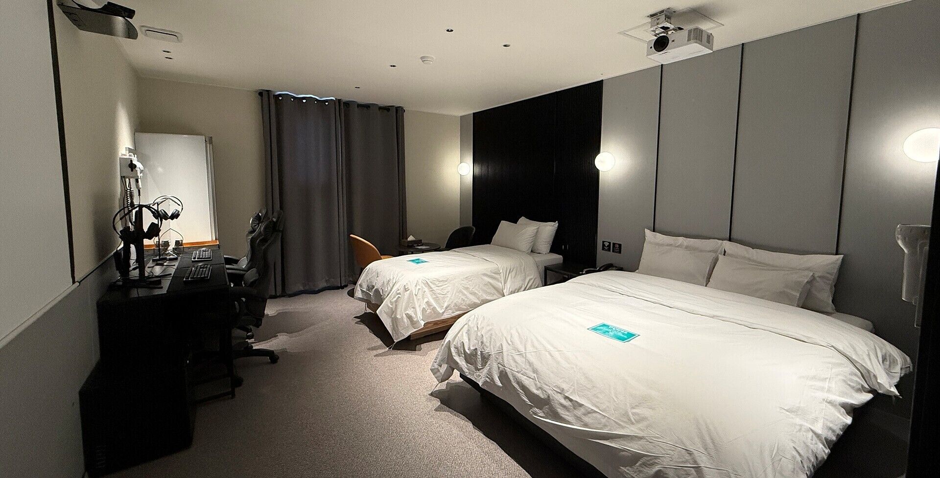 Una habitación de hotel con dos camas, un escritorio con computadora, una silla y una lámpara de escritorio.