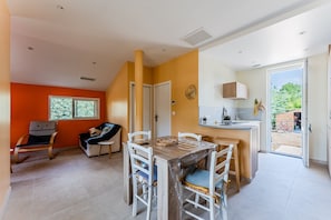 A modern kitchen with a dining area, a view to the outside, and a small seating area with a chair and a sofa.