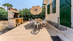 Eine Terrasse im Freien mit Tisch, Stühlen, einem Grill und einem Sonnenschirm.
