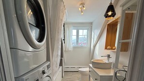 A laundry room with stacked washers and dryers, a window with a view, and a sink with a mirror above it.