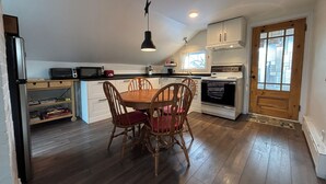 A kitchen with wooden flooring, a dining table with chairs, a microwave, a toaster, and a stove.