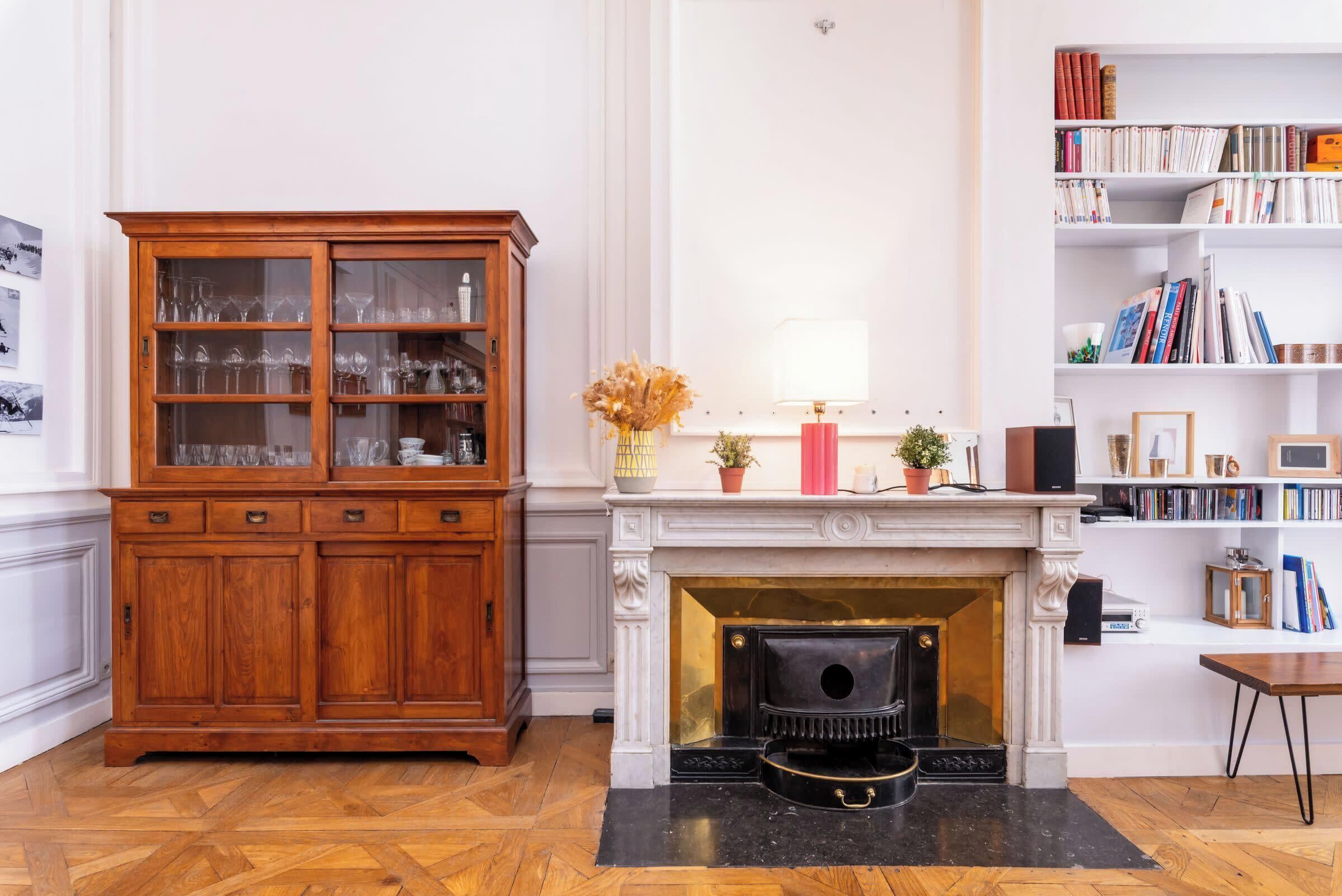 Een kamer met een houten kast, een open haard en een boekenplank.