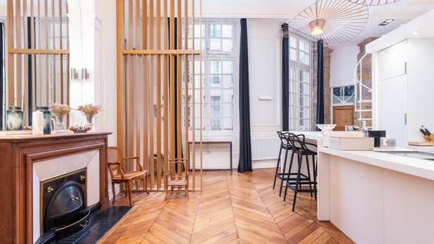 A modern kitchen with a herringbone wood floor, a fireplace, wooden slats, and a bar area with stools. - Le Central - 200 m² apartment in the heart of the city (Lyon)
