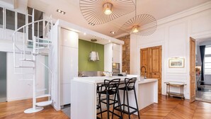 A modern kitchen with a central island, white cabinetry, a green accent wall, and a spiral staircase. - Le Central - 200 m² apartment in the heart of the city (Lyon)